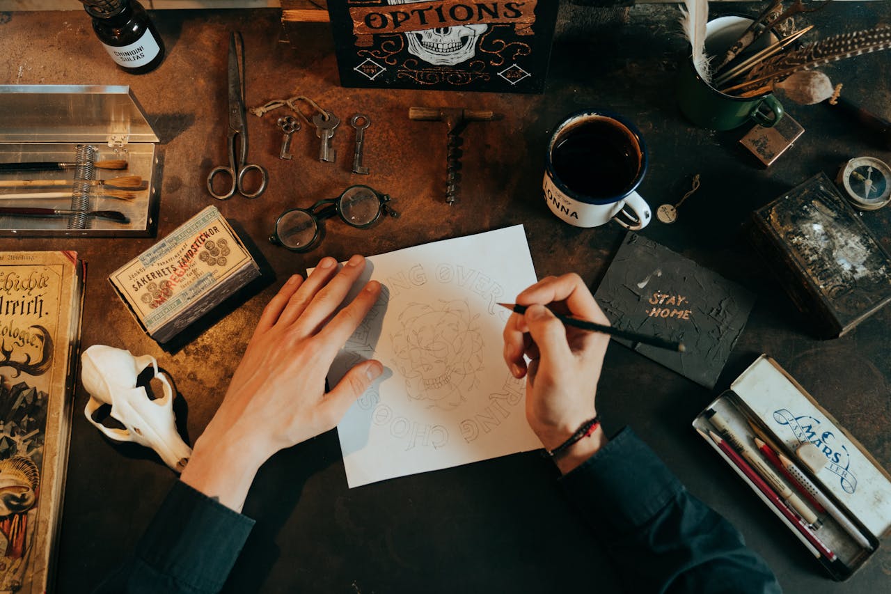 A top view of a vintage workspace with drawing tools, skull, and scattered items on a rustic desk.